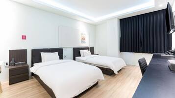 A hotel room with two beds, a desk, a chair, a flat-screen TV, and a window with curtains.