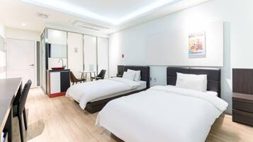 Ein Hotelzimmer mit zwei Betten, einem Schreibtisch, einem Stuhl und einer kleinen Küchenzeile.