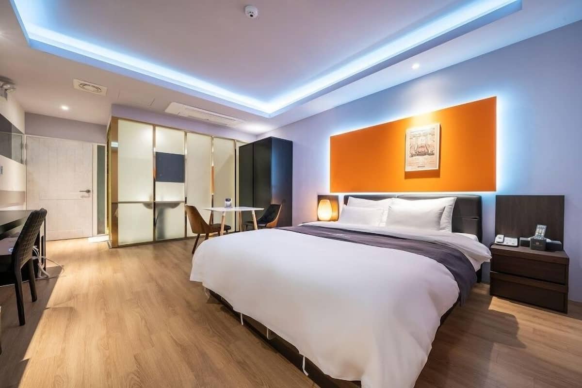 A modern hotel room with a large bed, a desk, and a seating area.