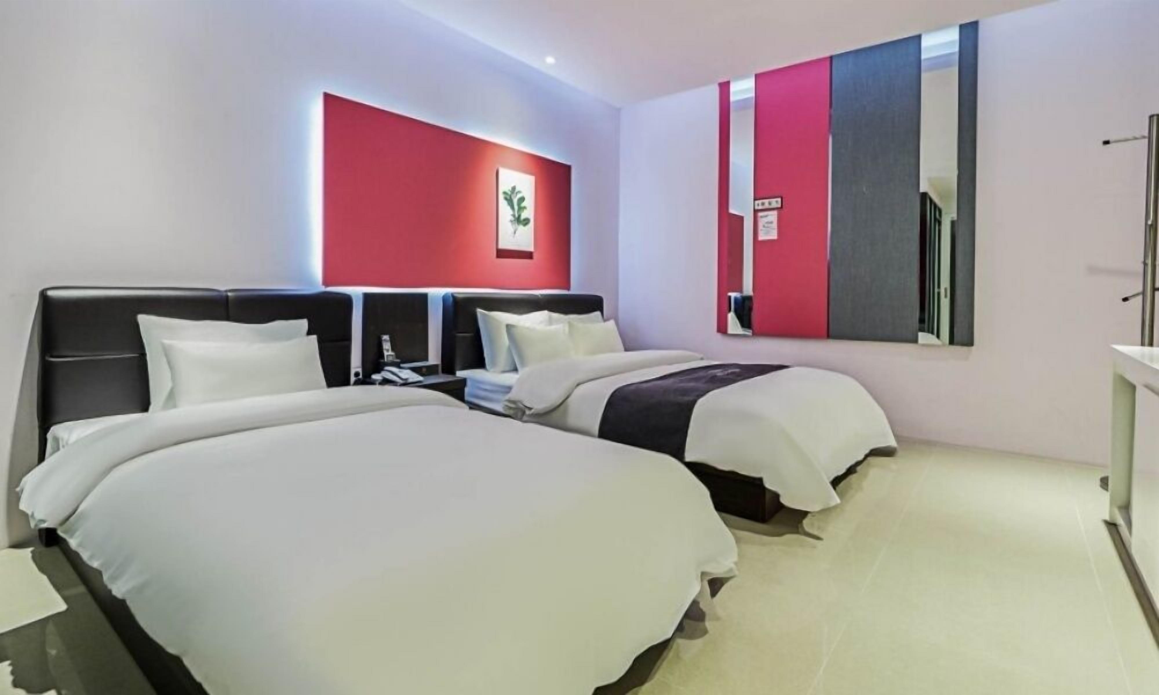 Una habitación de hotel con dos camas, una pared de acento roja, un espejo grande y un diseño moderno.