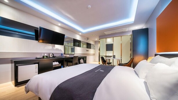 A modern hotel room with a large bed, a desk, a flat-screen TV, and a bathroom with a mirror and toilet. - Gimpo Pentastar Hotel (Gimpo)
