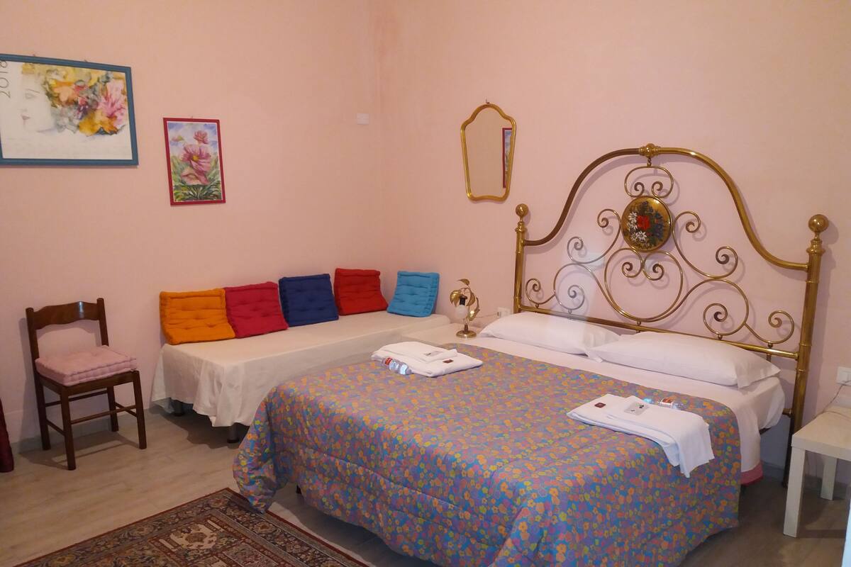 A bedroom with a bed, a chair, a nightstand, and a wall with two framed pictures.