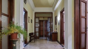 Um corredor com piso de mármore, portas de madeira e um vaso com planta.