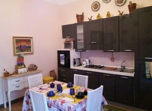Cocina compacta con gabinetes oscuros, microondas, estufa y pileta. Hay una mesa de comedor con sillas y un mantel colorido.