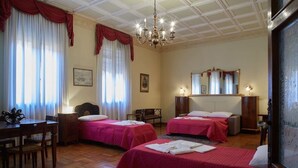 Quarto de hotel com duas camas, uma escrivaninha de madeira, um candelabro e um espelho grande.