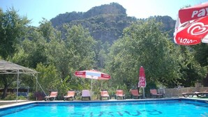 A swimming pool with lounge chairs and umbrellas, surrounded by lush greenery and a mountainous backdrop. - Sirius Hotel (Ortaca)