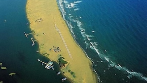 An aerial view of a coastal area with a sandy beach, clear blue waters, and a mountainous backdrop. - Sirius Hotel (Ortaca)