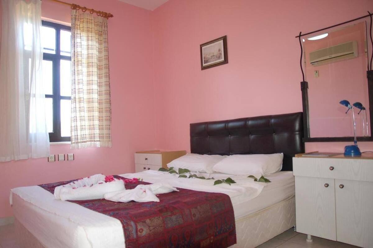 A bedroom with a bed, a bedside table, a wardrobe, a window with curtains, and an air conditioning unit.