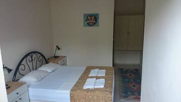 A single bed with a mattress, pillows, and a blanket. There is a small bedside table with a lamp. A colorful artwork hangs on the wall. A wardrobe is visible in the background.