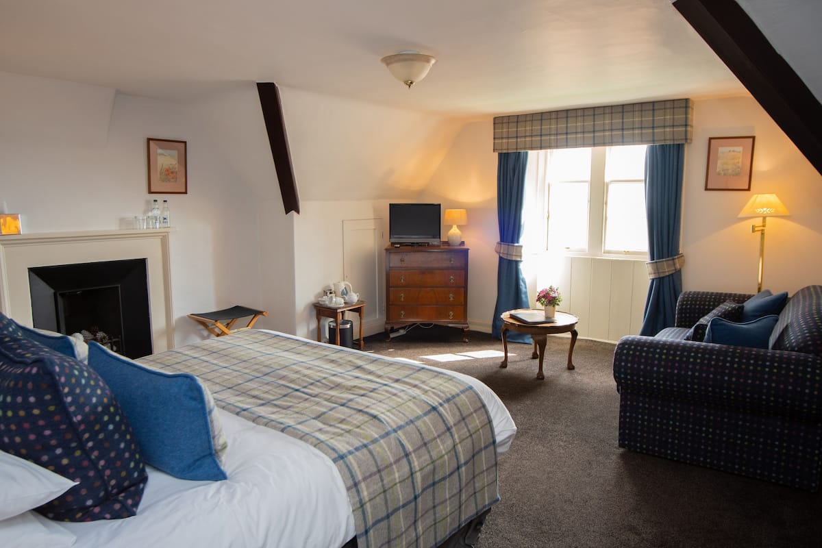 A hotel room with a bed, a sofa, a television, a fireplace, and a window with curtains.