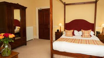 A four-poster bed with a red headboard, a wooden wardrobe, and a vase of flowers on a nightstand.