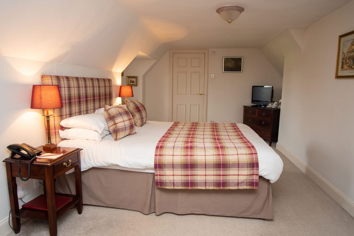 A bedroom with a bed, two bedside lamps, a nightstand with a phone, a dresser, and a television.