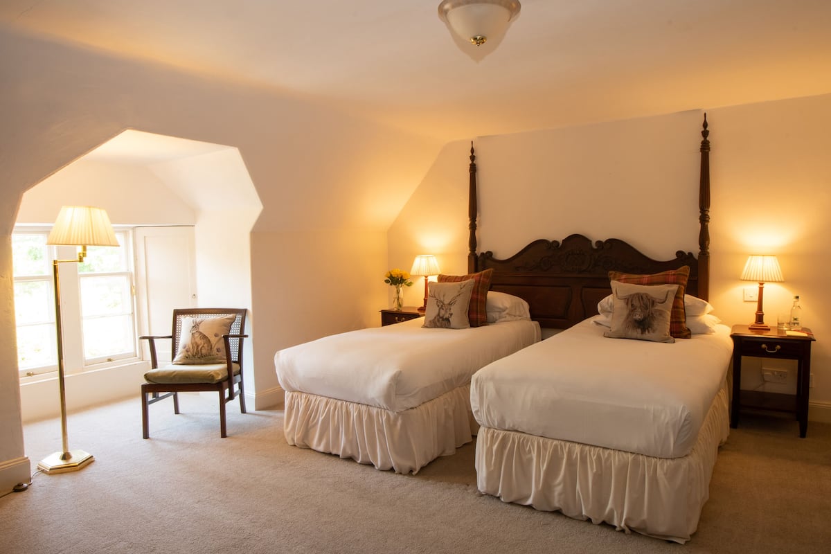 A bedroom with two beds, a chair, and a nightstand with lamps.