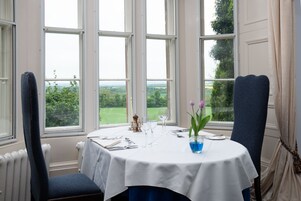 Mesa de comedor para dos con vistas al campo a través de amplios ventanales.