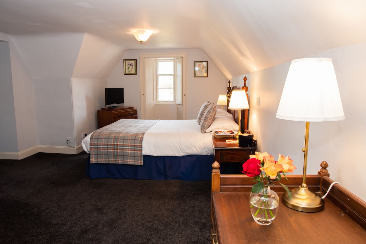 A bedroom with a bed, bedside table, lamp, and a vase with flowers.