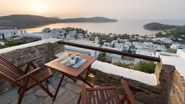 Une terrasse avec une table dressée pour le petit-déjeuner, donnant sur une ville côtière aux bâtiments blancs et offrant une vue sur la mer.