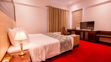 A hotel room with a bed, a desk with a lamp, a television, and a red carpet.