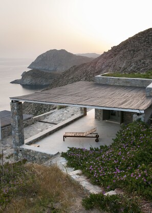 A coastal building with a stone exterior, a wooden bench, and a view of the sea. - Serifos Houses Kalo Ampeli (Serifos)