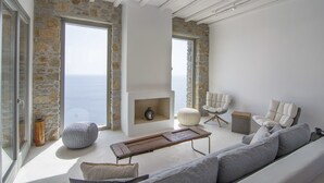 Un vaste espace de vie agrémenté d’un mur en pierre, d’une cheminée, d’un canapé et offrant une vue sur la mer.