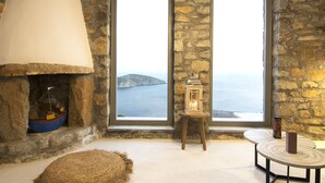 Une pièce chaleureuse avec un mur en pierre, une grande fenêtre donnant sur la mer, un luminaire suspendu et une petite table sur laquelle est posée une lanterne.