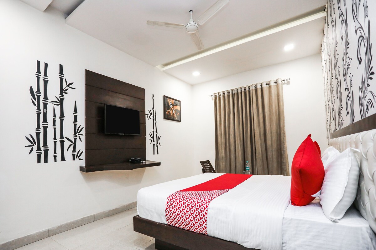 A hotel room with a bed, a mounted TV, a wall-mounted shelf, and a ceiling fan.