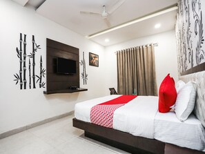 A hotel room with a bed, a mounted TV, a wall-mounted shelf, and a ceiling fan. - OYO 3301 Maya International (Kolkata)