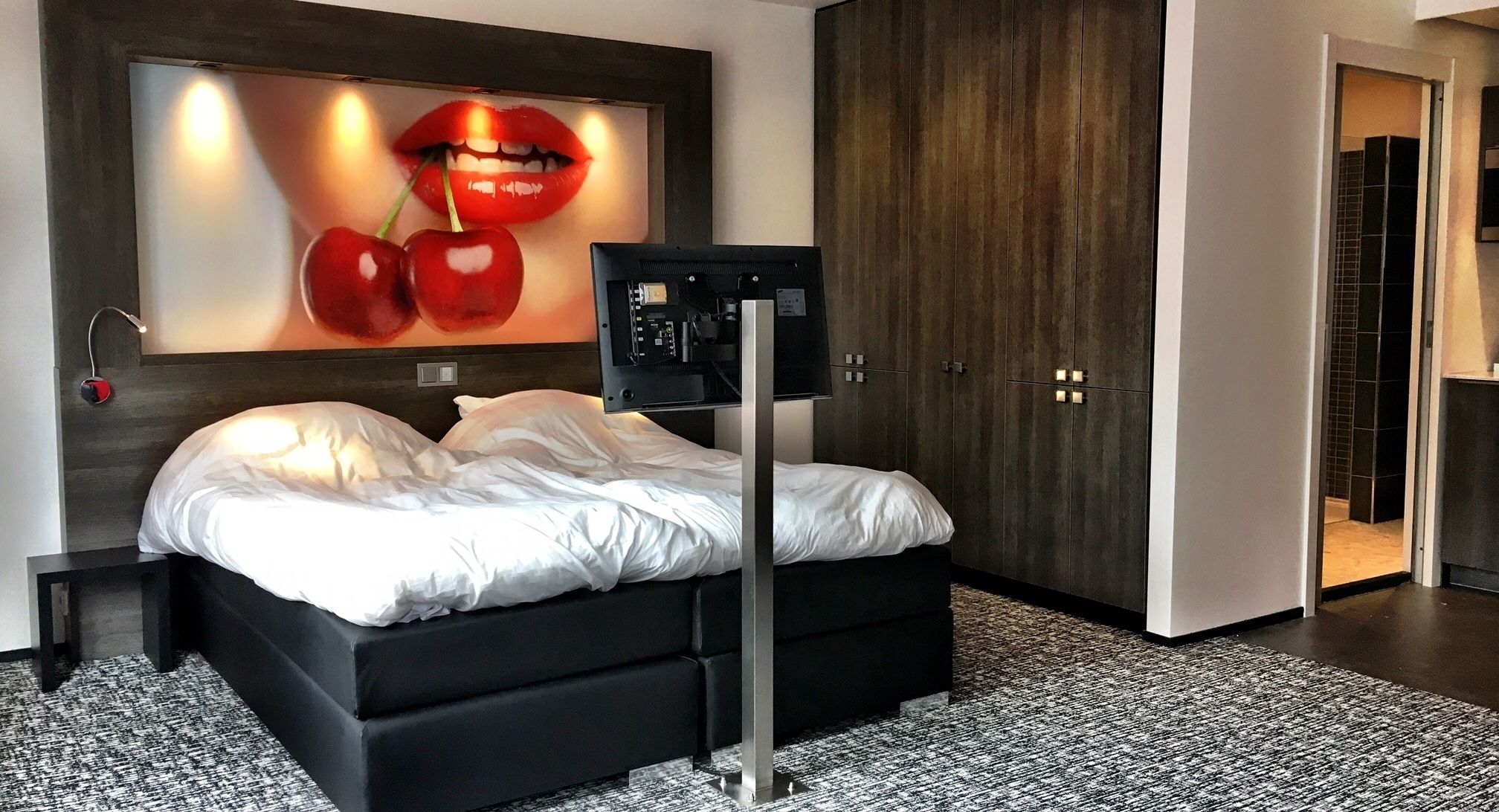A modern bedroom with a large bed, a wall-mounted TV, and a wardrobe.