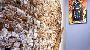 A staircase with a wooden handrail leading to a room with a textured stone wall and a colorful abstract painting on the wall. - Apart Food and Drinks (Zwolle)