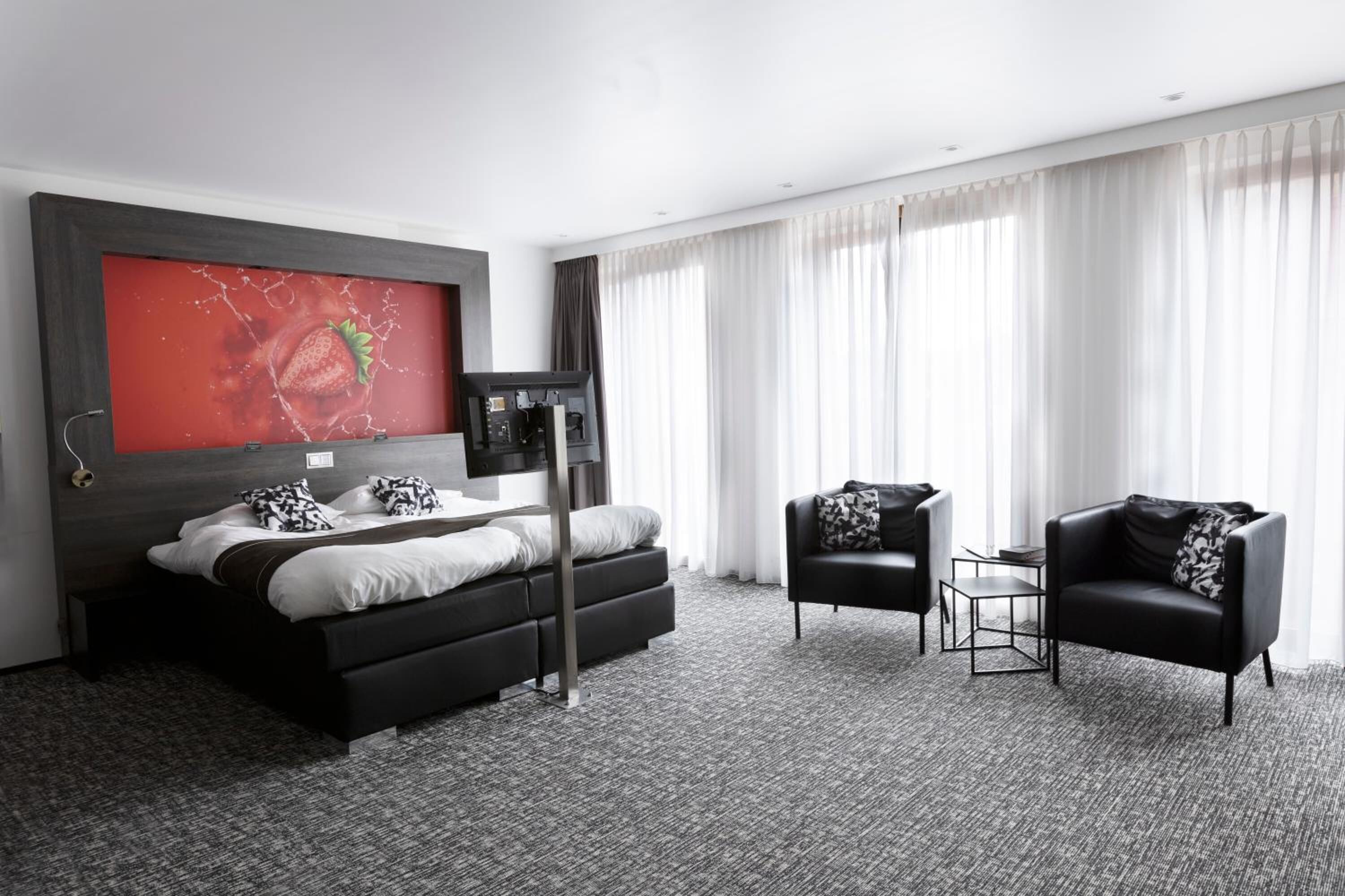 A modern hotel room with a large bed, a coffee machine, a sofa, and a large window with curtains.