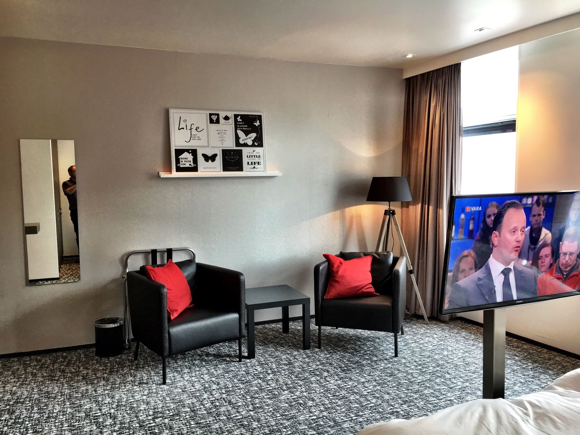 Ein Hotelzimmer mit zwei schwarzen Sesseln, einem kleinen Tisch, einem Fernseher und einer Wand mit Motivationspostern.