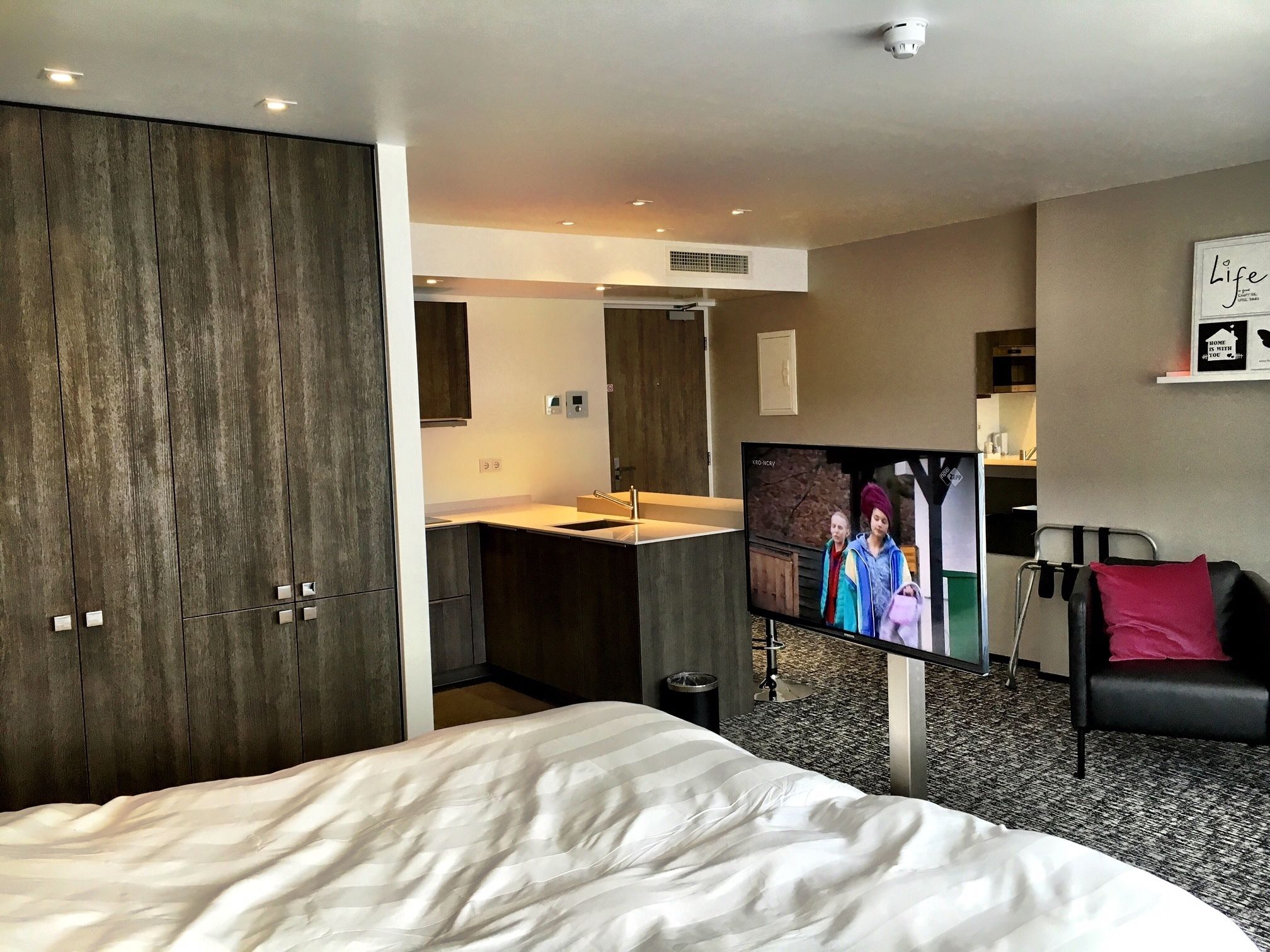 A hotel room with a bed, a TV, a desk with a sink, and a chair.