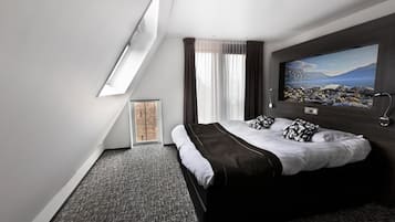 Quarto de hotel moderno com uma cama grande, um quadro na parede e um claraboia.
