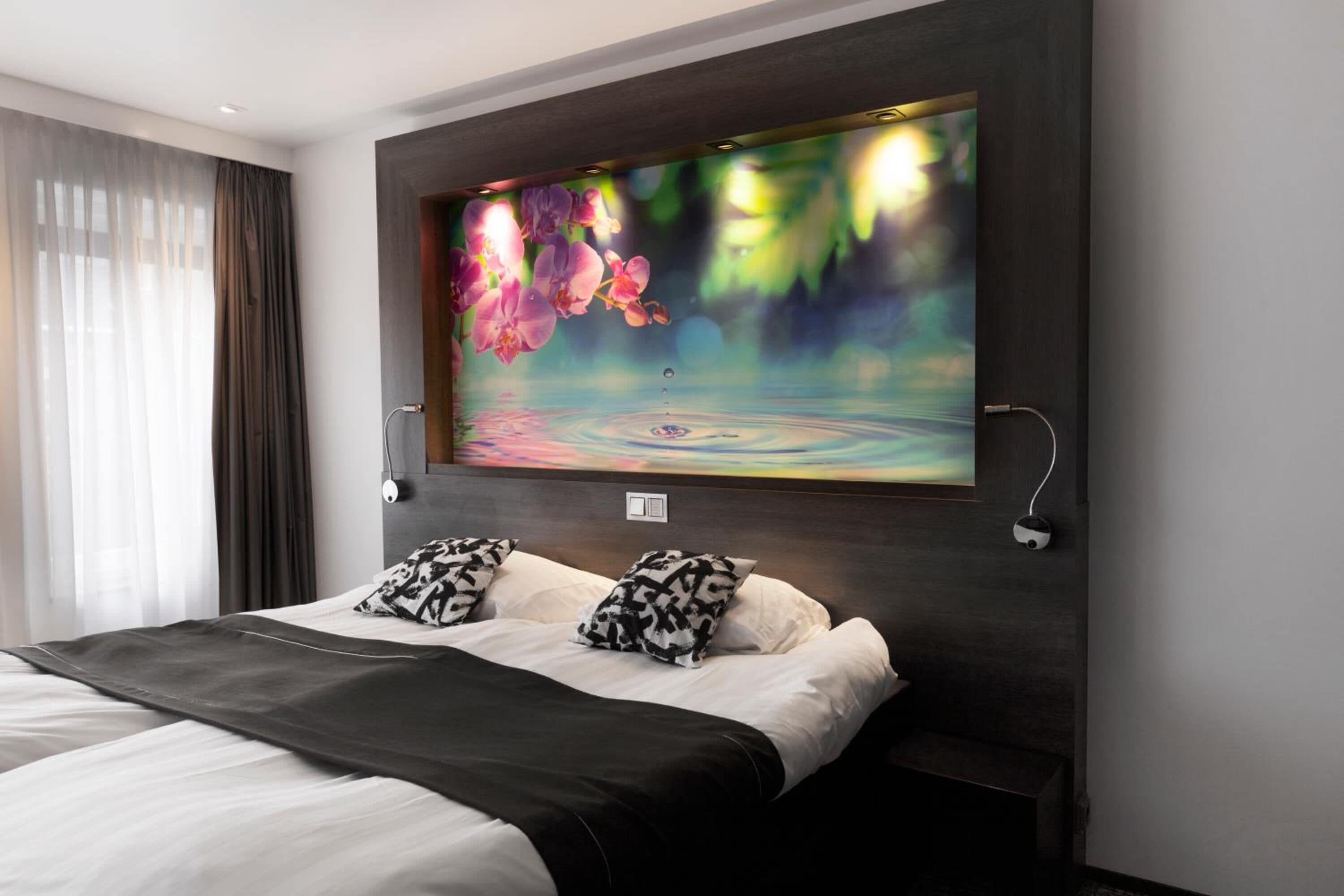 Una habitación de hotel moderna con una cama grande, un televisor montado en la pared y un ventanal con cortinas traslúcidas.