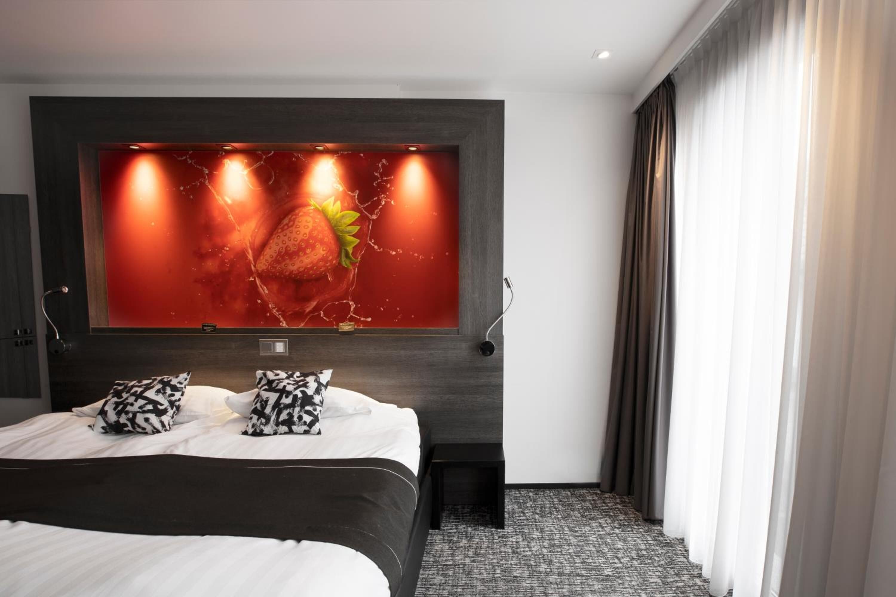 Habitación de hotel moderna con una cama grande, televisor montado en la pared y cabecera de madera oscura.