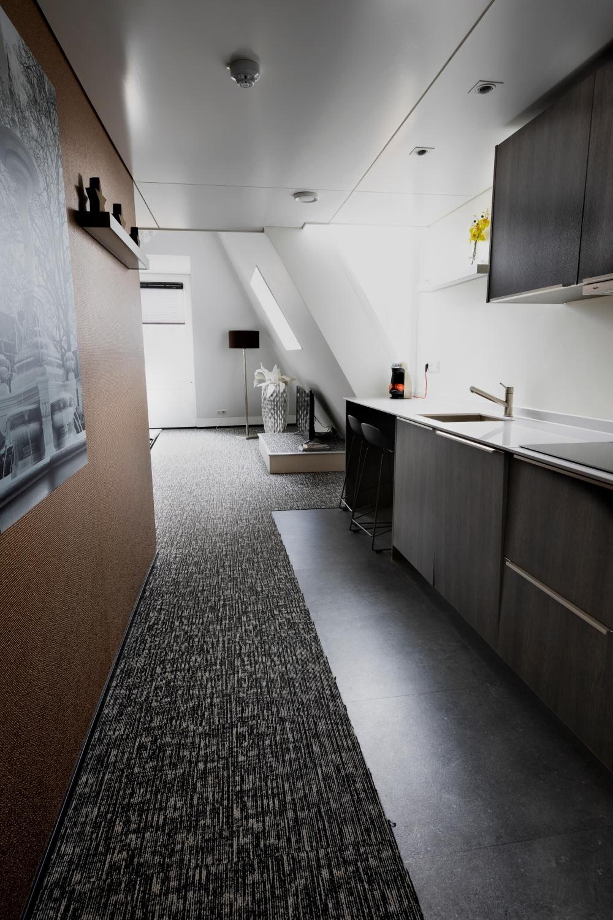 Una cucina moderna con mobili scuri, un piano di lavoro bianco e un forno integrato. Sullo sfondo, si intravede una piccola area bar con degli sgabelli.