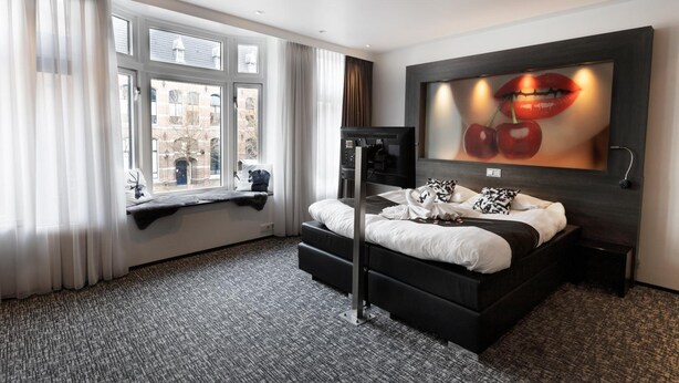 A modern hotel room with a large bed, a TV, and a window with curtains. - Apart Food and Drinks (Zwolle)