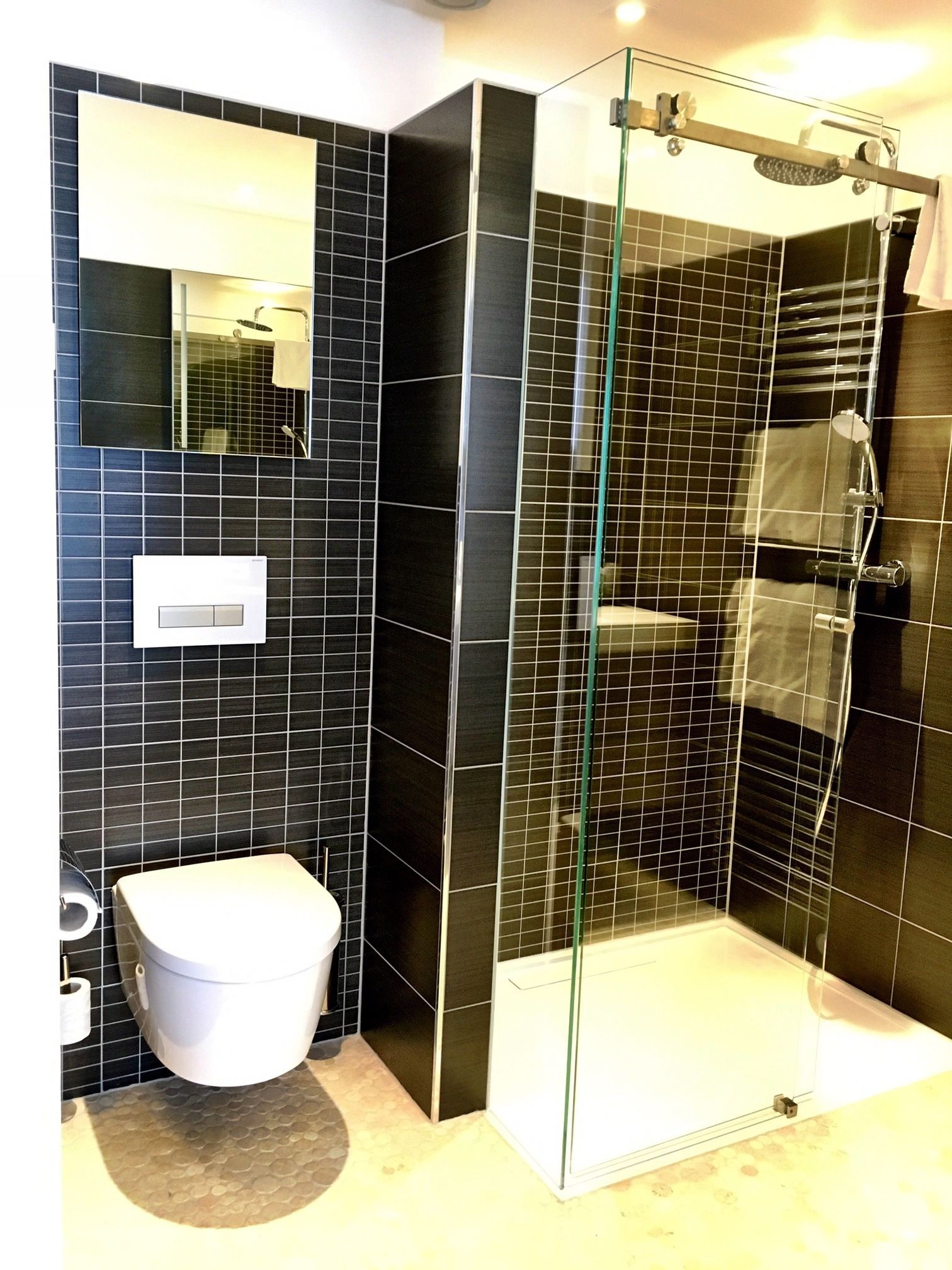 Une salle de bain moderne avec une douche à parois de verre, des toilettes blanches et un mur recouvert de carreaux.