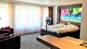 A hotel room with a bed, a desk, a chair, a TV, and a large window with curtains.