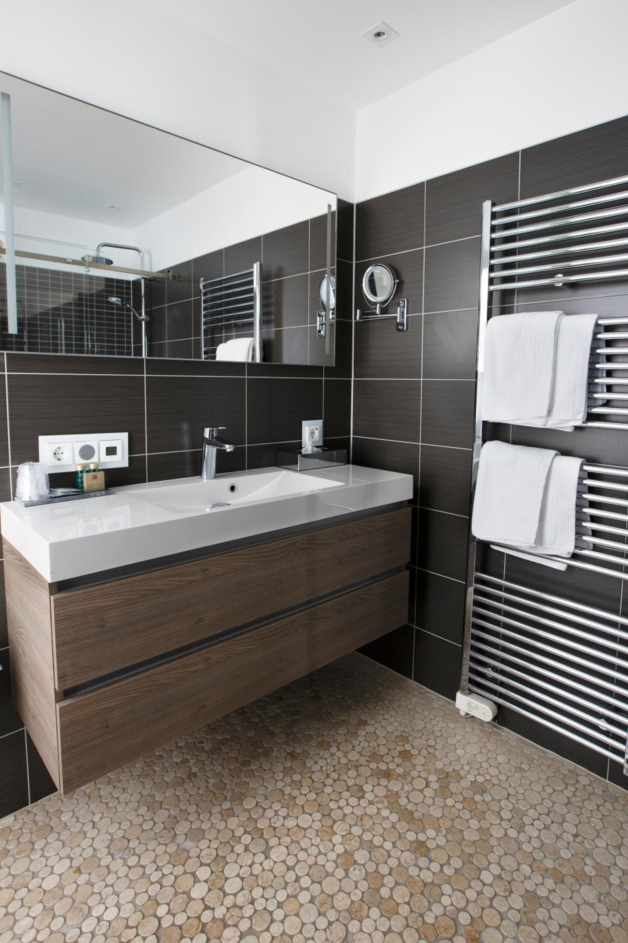 Une salle de bain moderne avec un grand miroir, un lavabo blanc et un porte-serviettes.