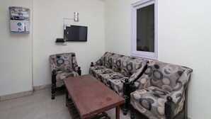 Una sala de estar con un sofá estampado, una mesa de centro de madera, un televisor de pantalla plana montado en la pared y un dispensador de agua.