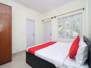 Ein Schlafzimmer mit Bett, Schrank und einem Fenster mit Blick ins Grüne.