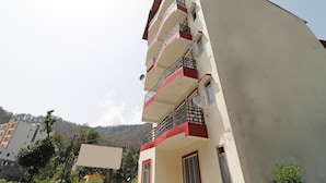 Un edificio de varios pisos con balcones, antenas parabólicas y montañas al fondo.