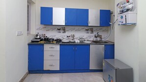 Una cocina con armarios azules y blancos, un protector contra salpicaduras de mármol y un refrigerador pequeño.