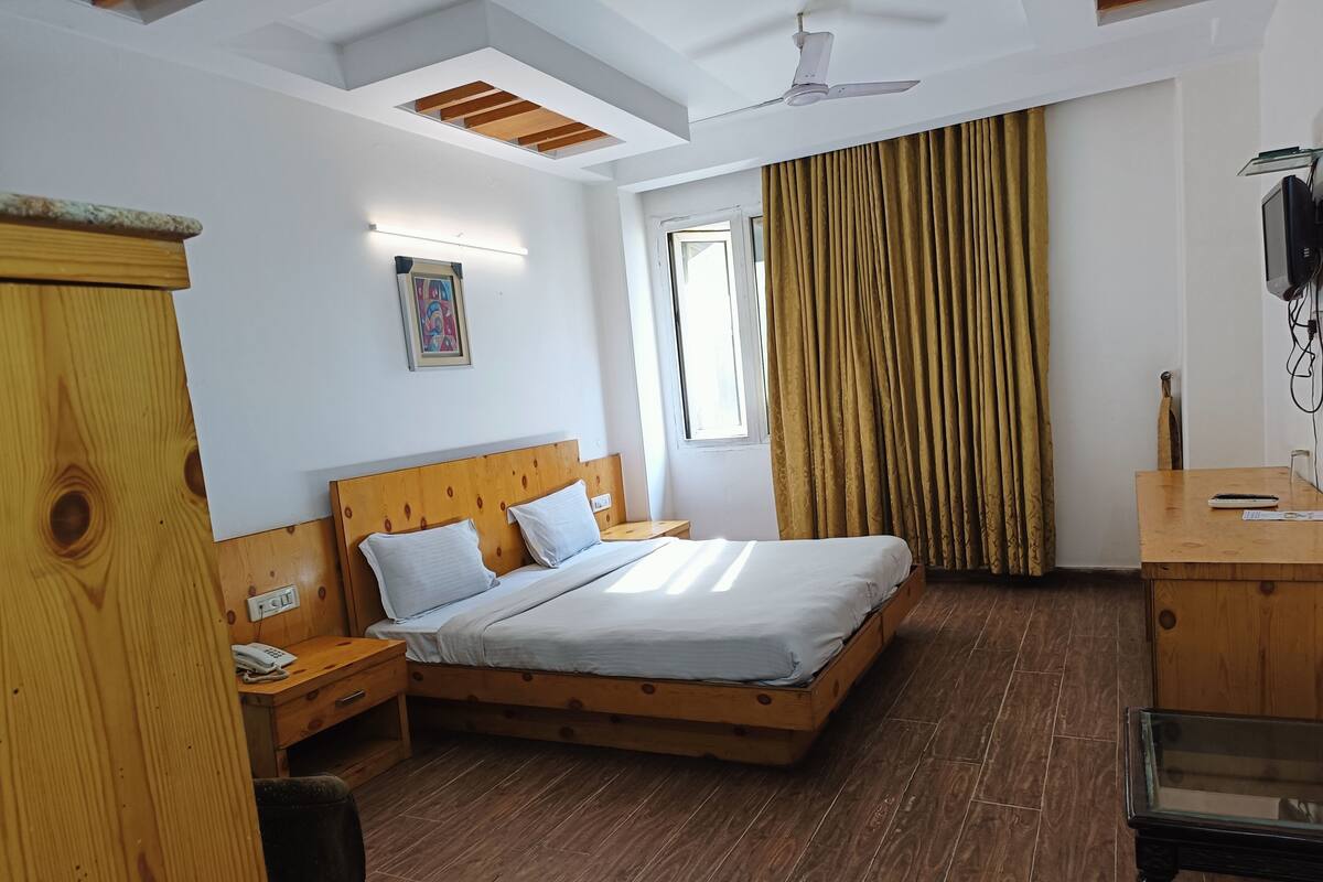 A bedroom with a wooden bed, a desk, a chair, a telephone, and a ceiling fan.