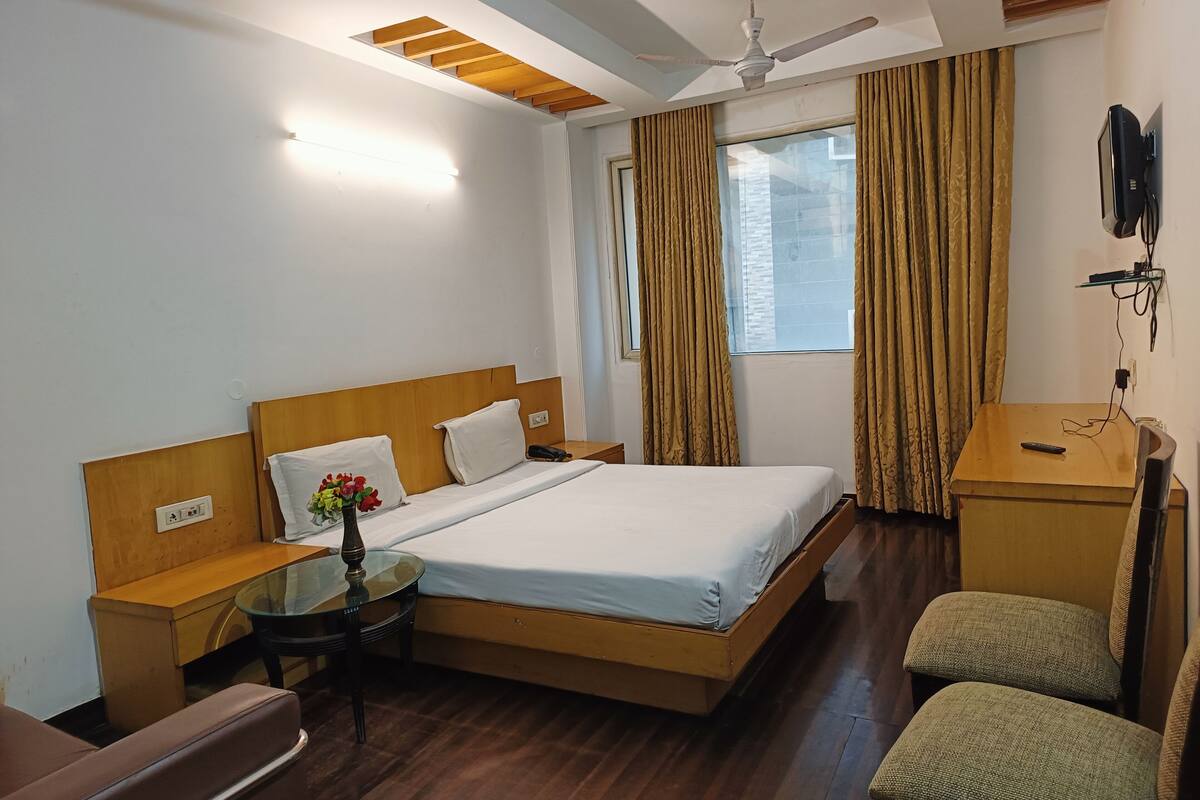 A hotel room with a bed, bedside table, chair, desk, and a ceiling fan.