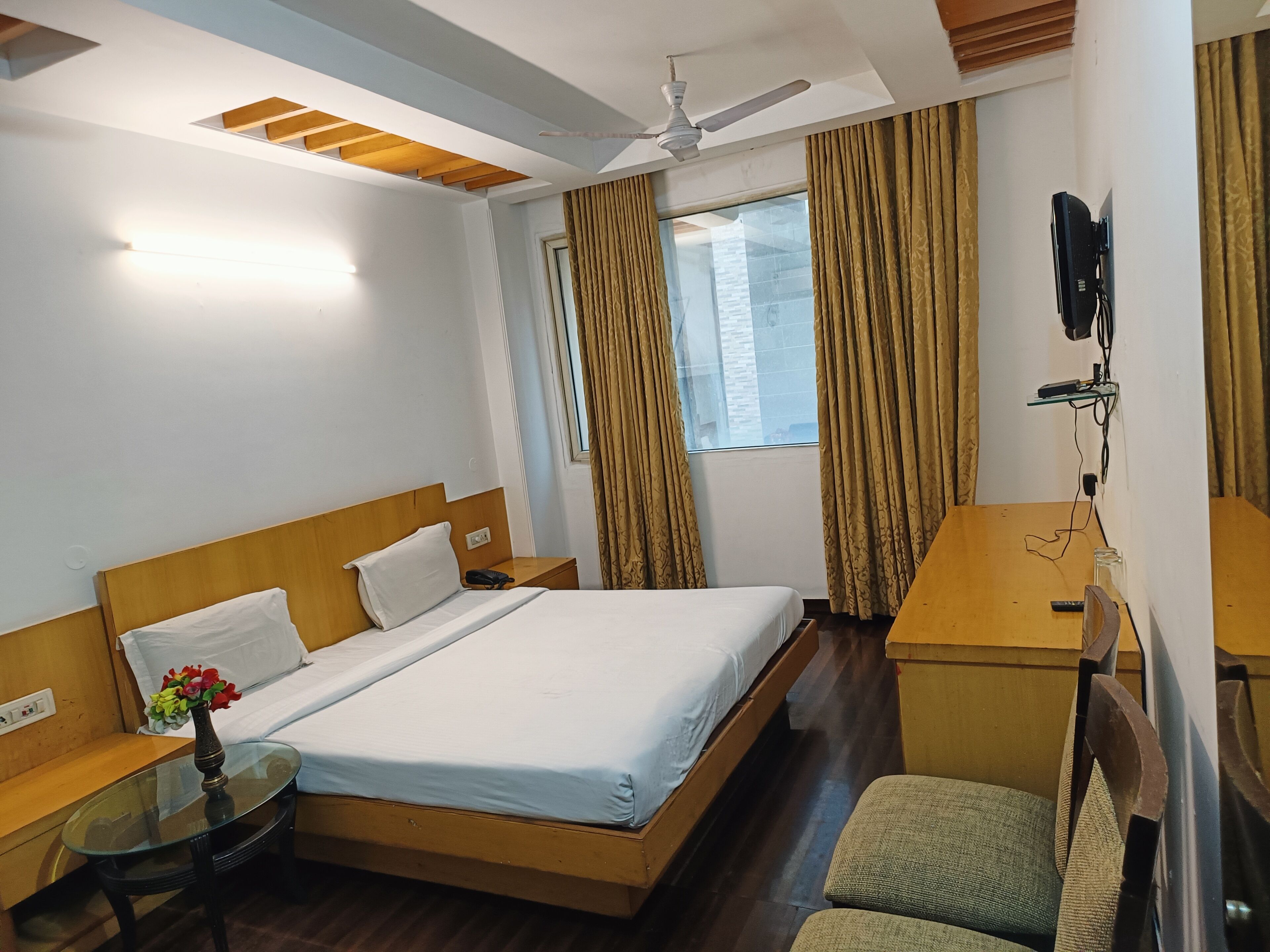 A hotel room with a bed, a desk, a chair, a TV, and a window with curtains.