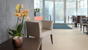 Ein Empfangsbereich mit einem modernen Sessel, einer Vase mit Orchideen und einer Glastür zum Essbereich.