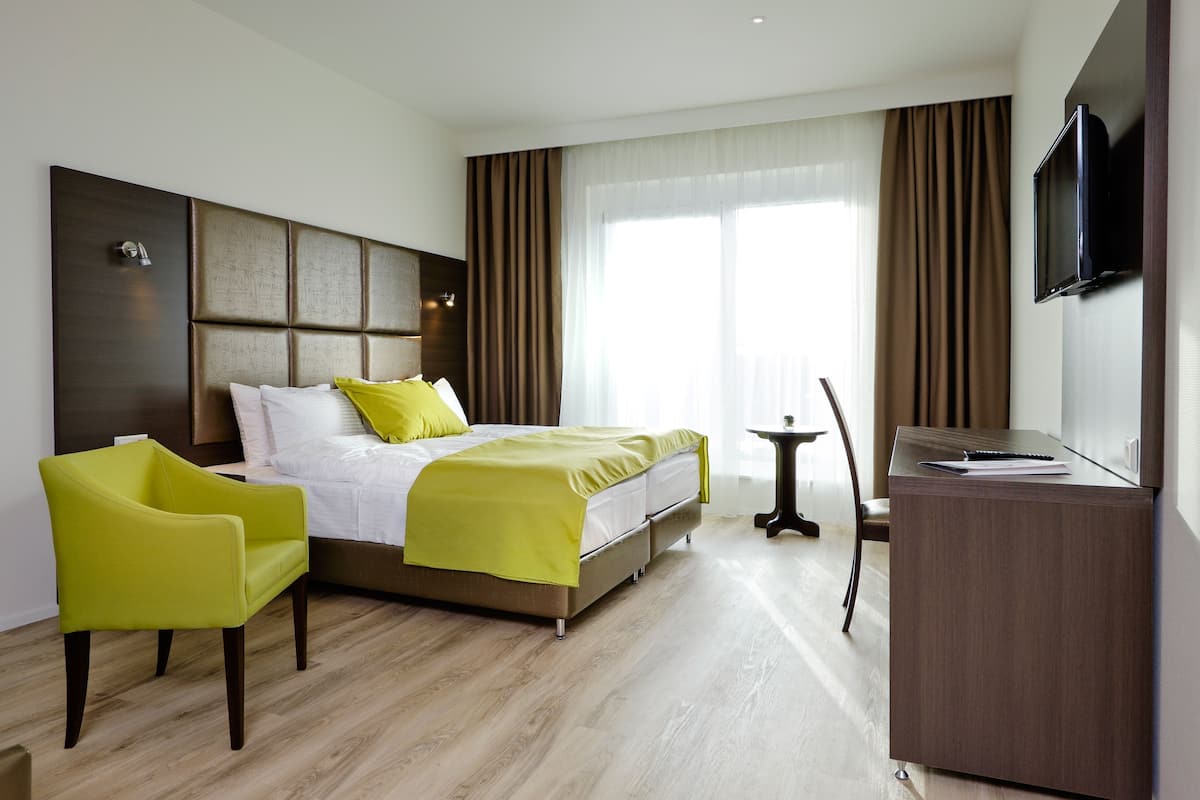 Ein Hotelzimmer mit Bett, Schreibtisch, Stuhl, Fernseher und einem fenster mit Vorhängen.