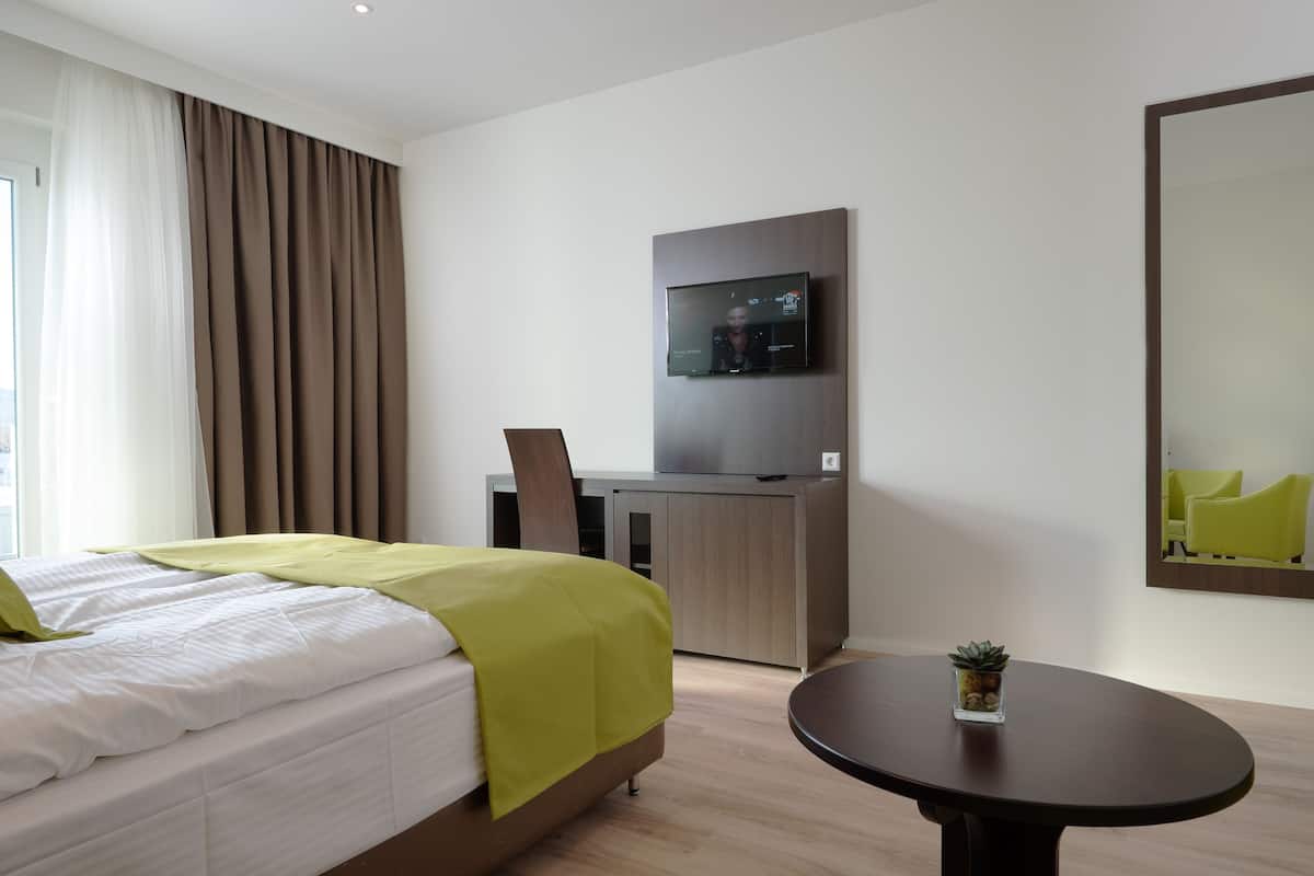 Ein modernes Hotelzimmer mit einem Bett, einem Schreibtisch, einem Fernseher und einem runden Tisch.