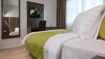 Una habitación de hotel con una cama grande, un escritorio, un televisor y un espejo.